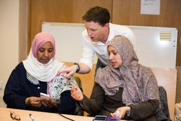 image of a man traing two women on use of an application on their mobile telephone